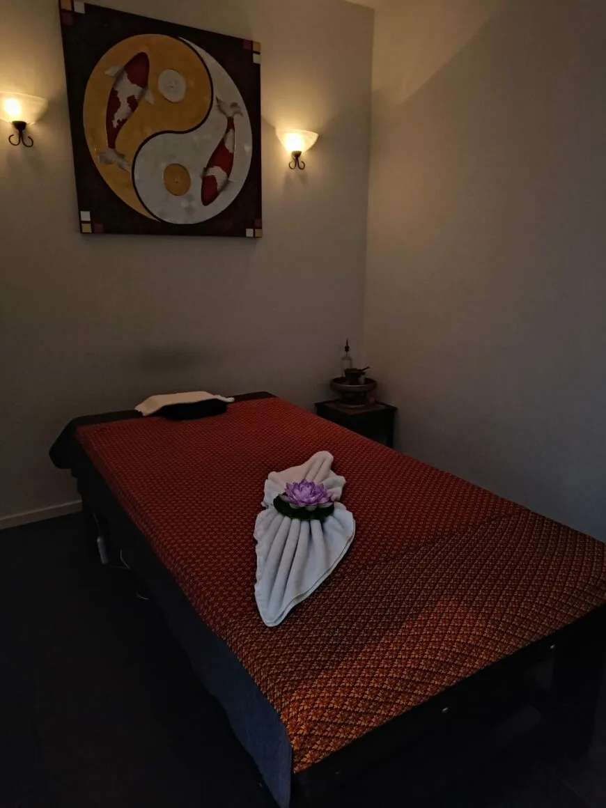 Behandelkamer met een massagetafel met rood Thais kleed, wandlampjes en een schilderij met koi.
