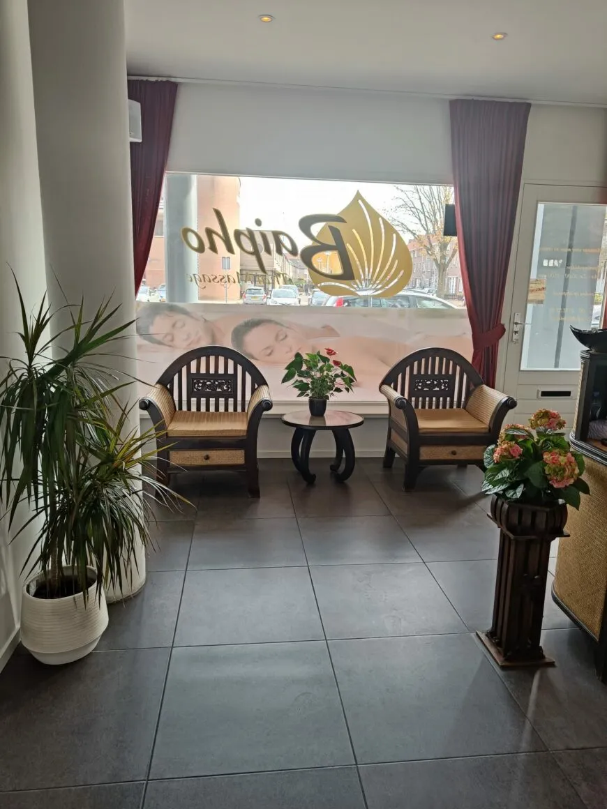 Wachtruimte met twee houten stoelen, een tafeltje met bloemen en het Baipho-logo op het raam.